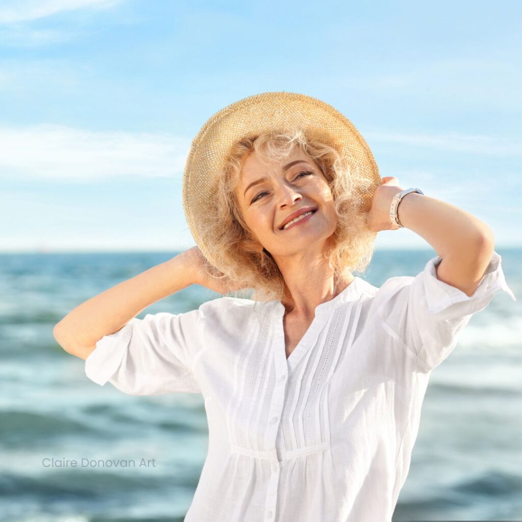 Mother Nature Offers Connection And Perspective - Happy older woman with curly hair, wearing a hat and smiling while standing in front of the ocean